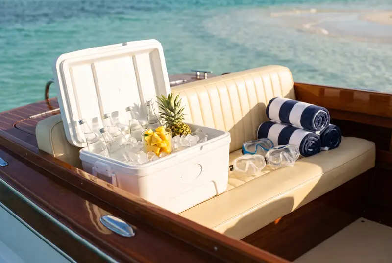 The stern bench of the boat with an open cooler of ice, snorkel masks and rolled striped towels.