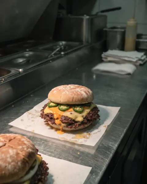 The Hot One: one smashed patty with pepper jack, jalapeño rings and orange chilli mayo, on the same counter.
