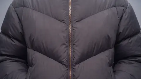 Close on the chest of the jacket: four chevron baffles meeting at the brass zip, in the same cool light.