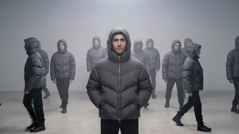 Film at 3 seconds: people in the same jacket walk out to the left and right while the man at the centre stands still.